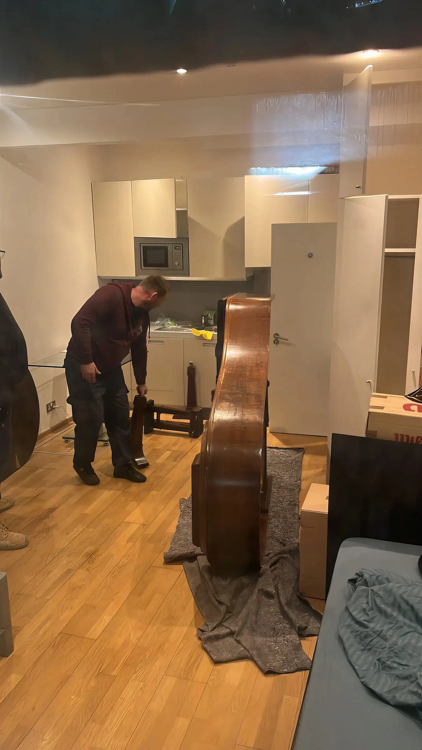 A mover putting the legs back on a baby grand piano in a kitchen