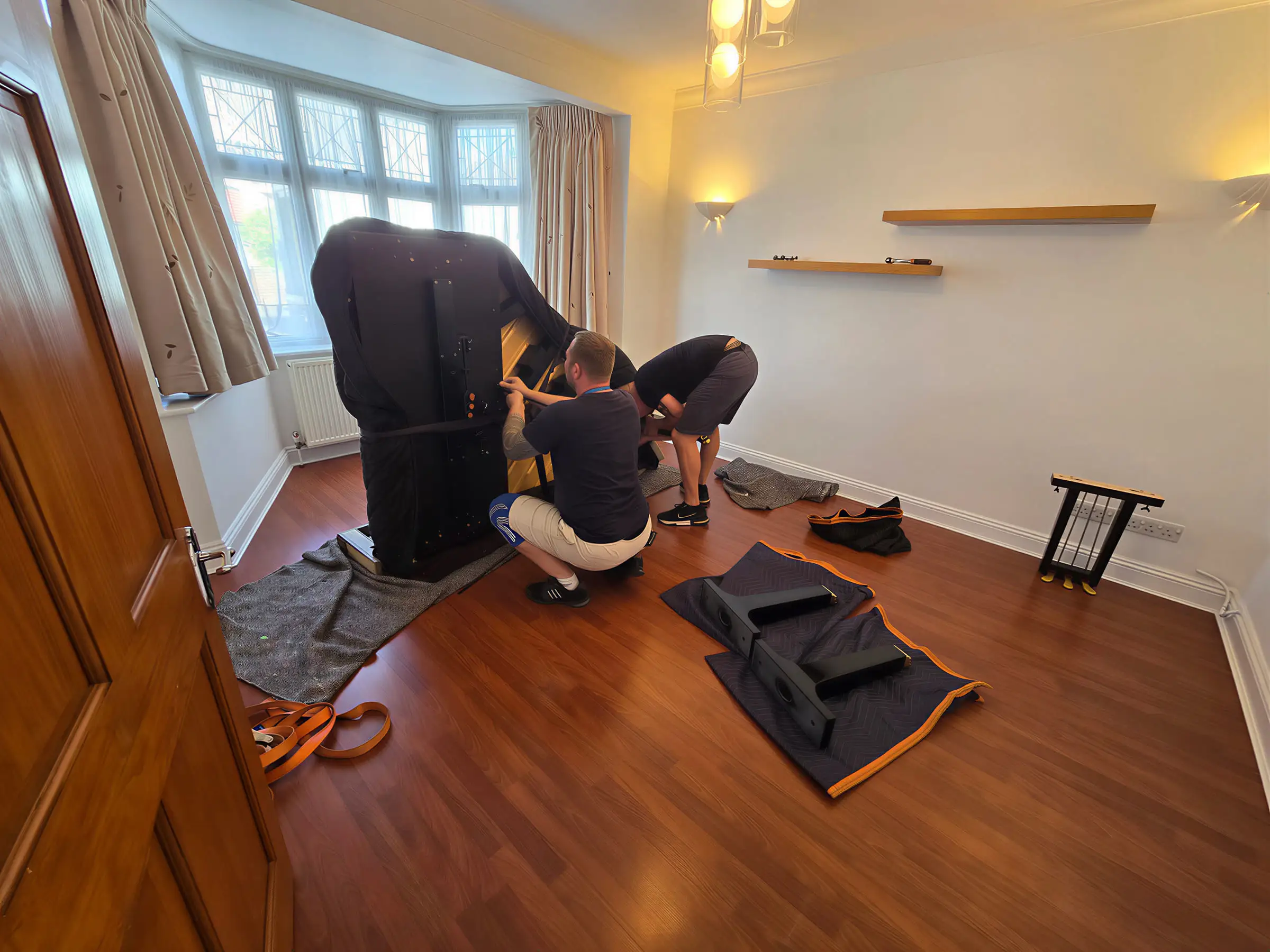 Two movers putting a grand piano back together on a living room floor