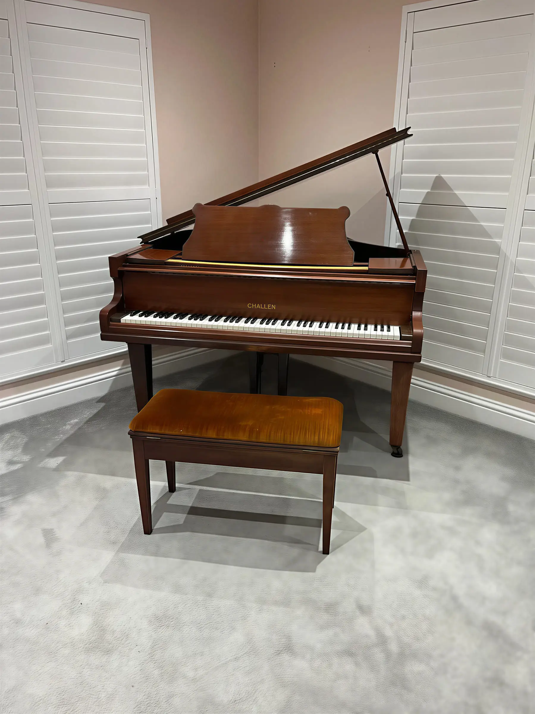 A Challen baby grand piano and its stool in a room with white shutters
