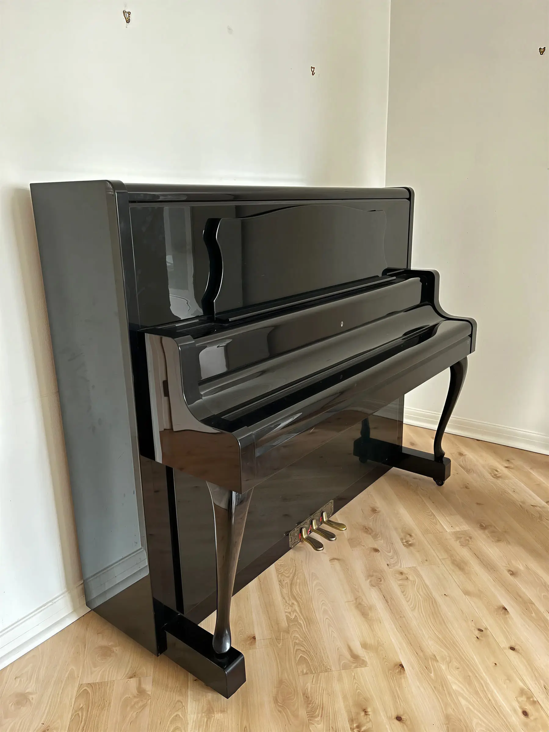 A black upright piano standing alone against the wall of an empty room