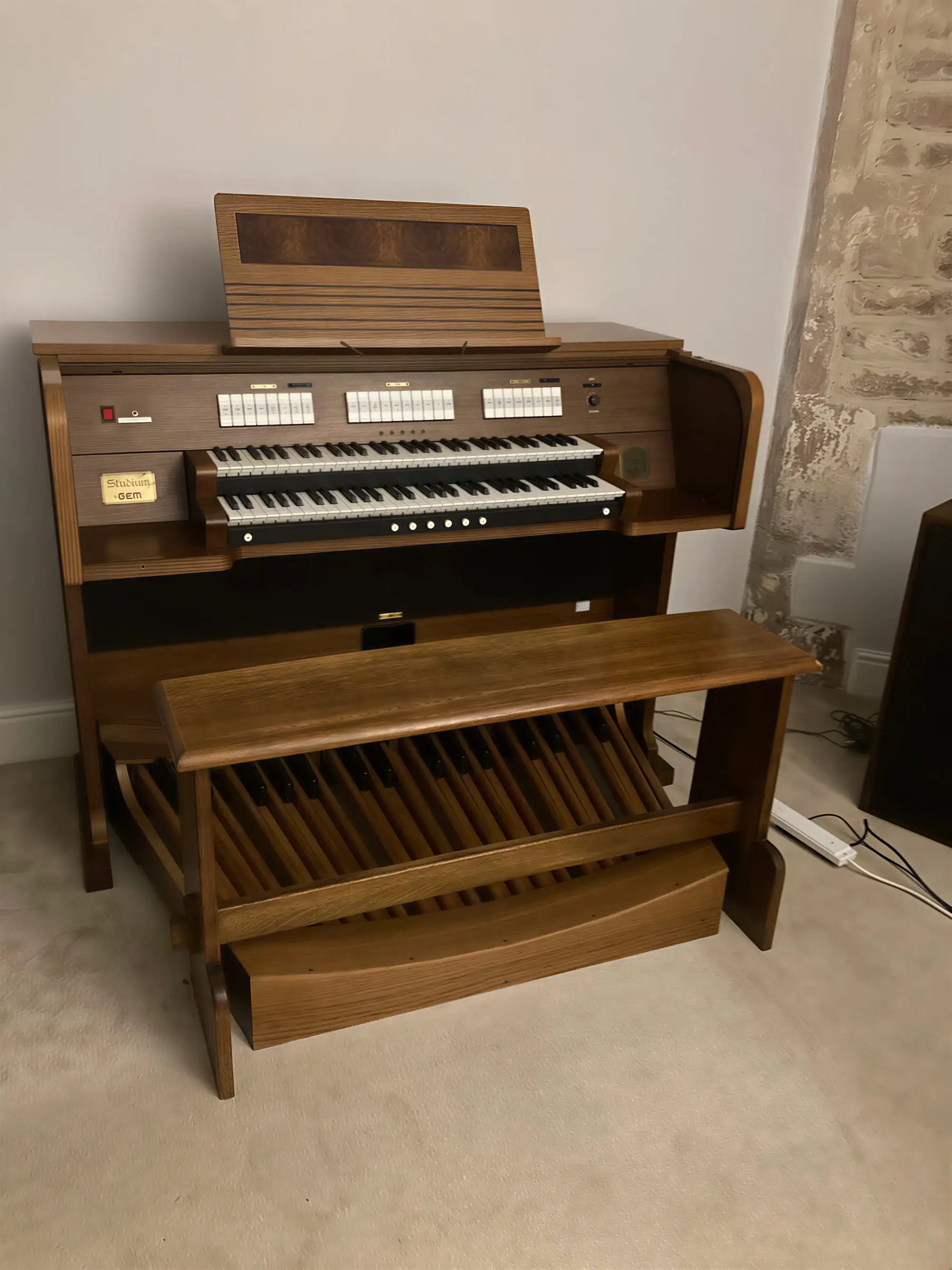 A wooden church organ with two keyboards and a pedalboard standing against a wall