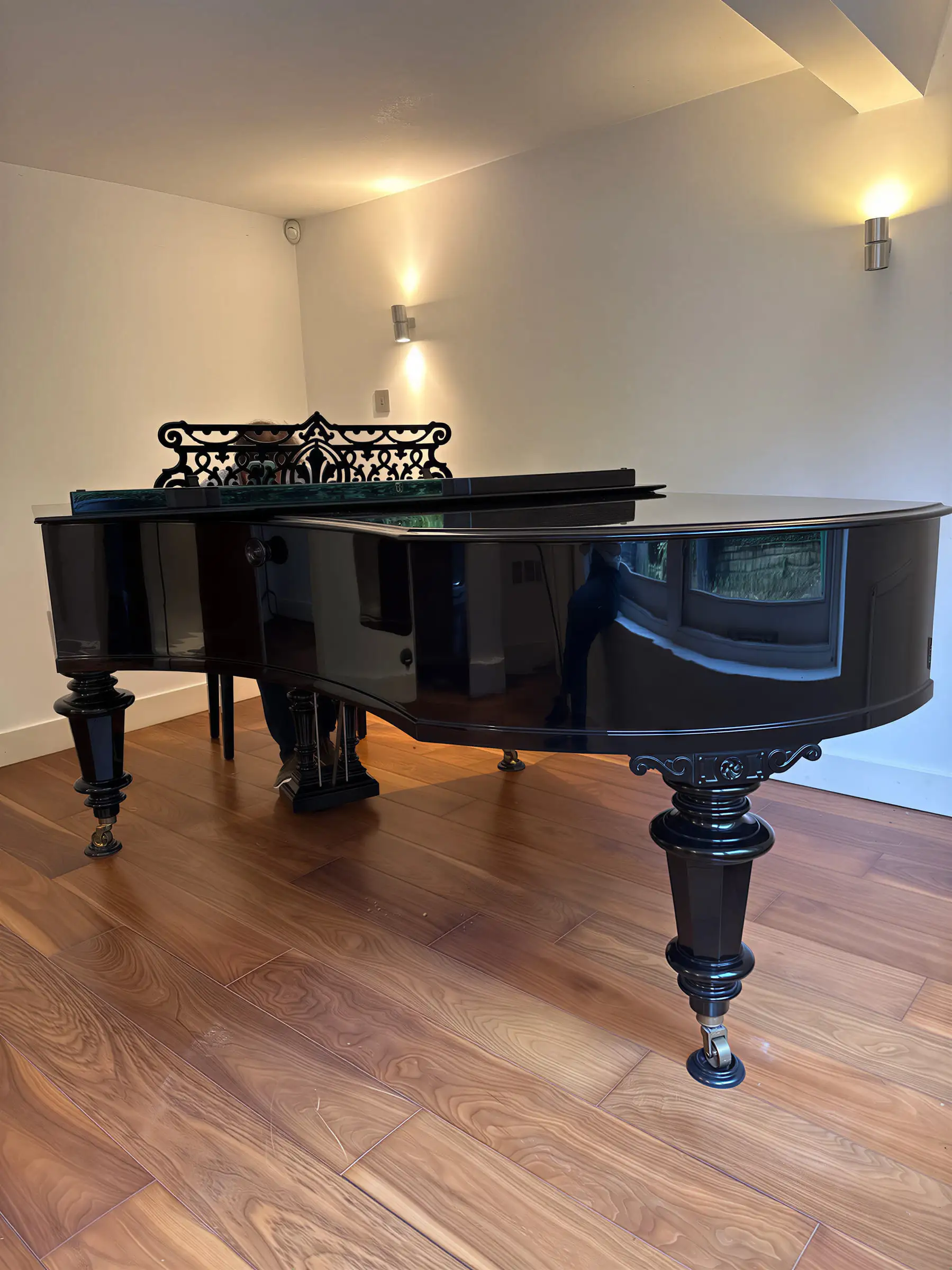 A black grand piano with an ornate music desk in a room with wall lights