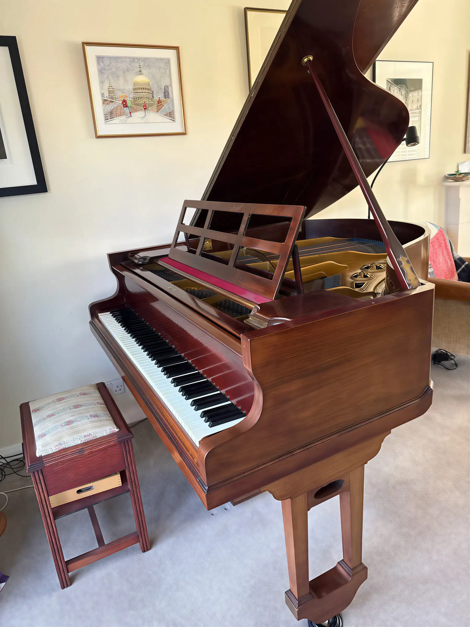 A mahogany grand piano with the lid raised beneath framed pictures