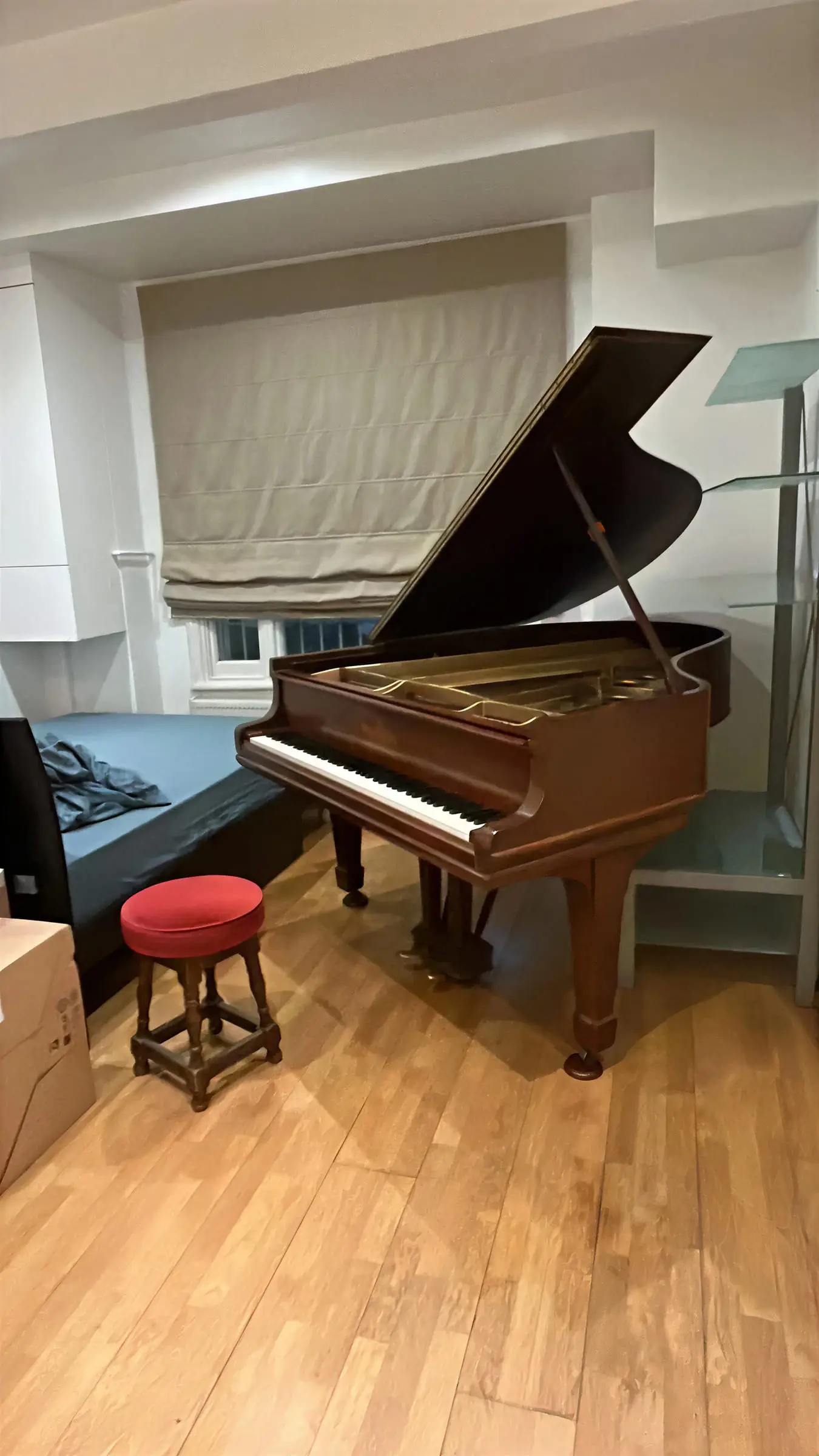 A mahogany baby grand piano with a red stool standing finished in a bright room
