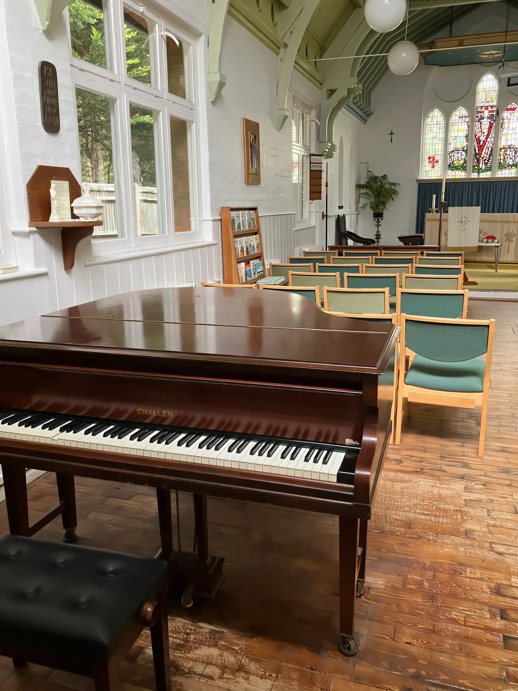 A grand piano in a church hall with rows of chairs behind it