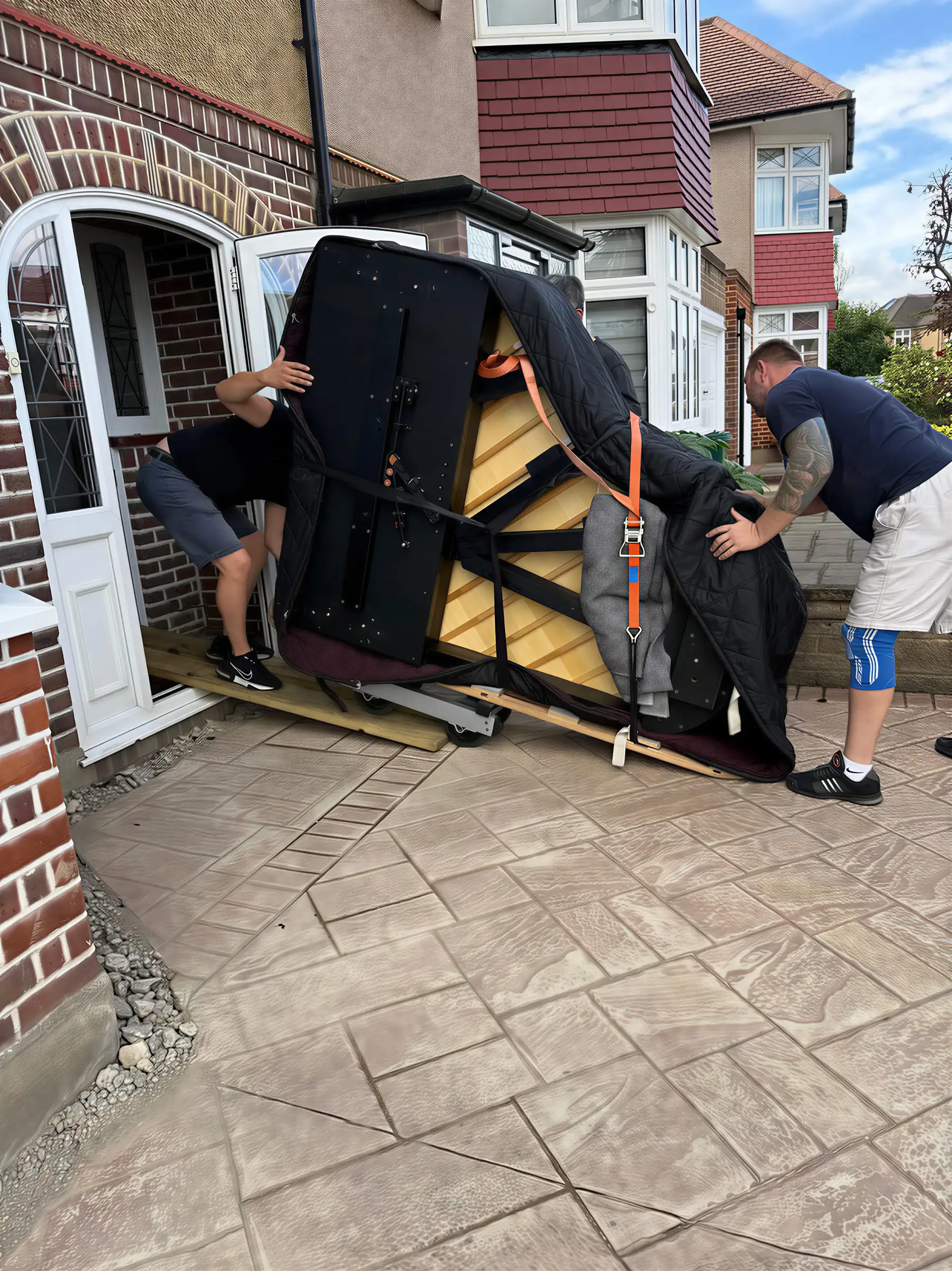 Two movers easing a grand piano on its side in through the front door of a house