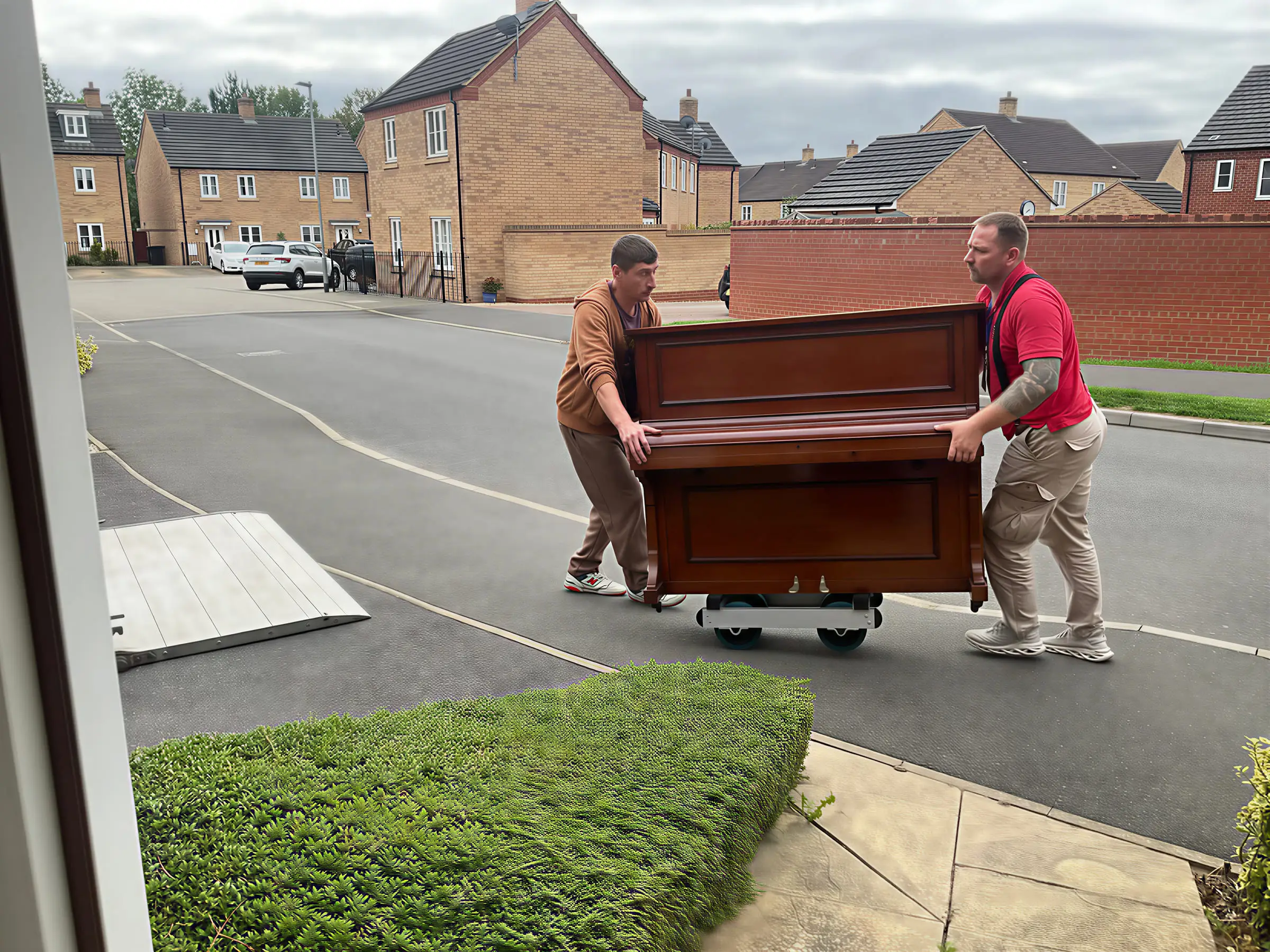 Two VVM movers wheeling an upright piano across a driveway towards the van