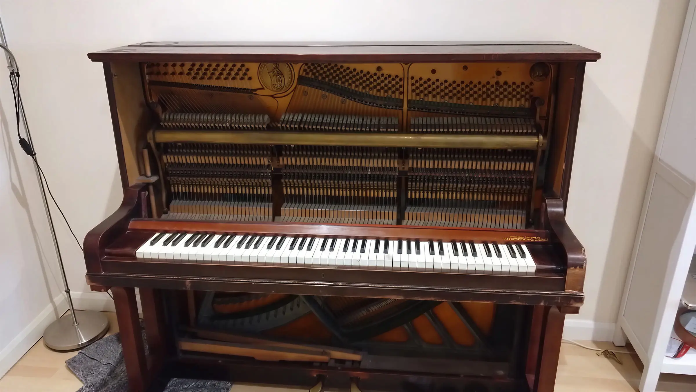 An old upright piano with its front panel off, showing the strings and hammers