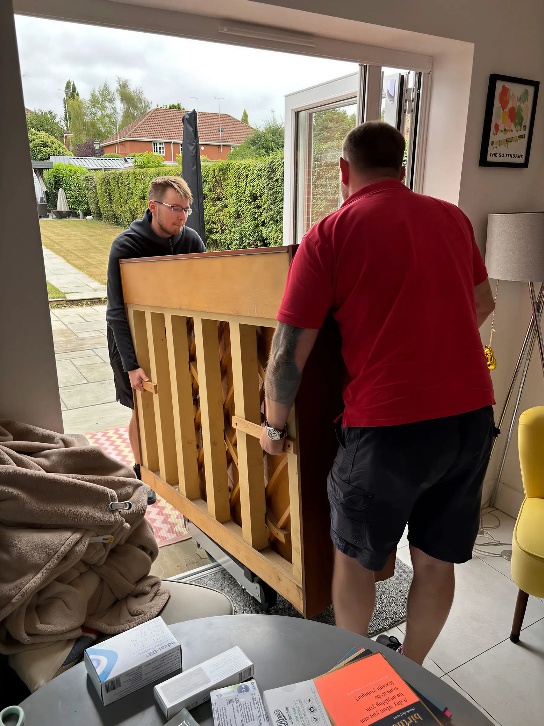 Two movers carrying the frame of an upright piano through a patio door