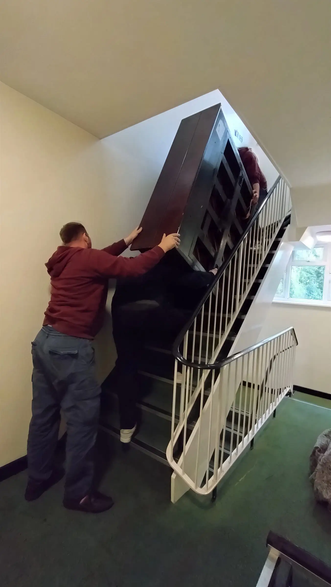 Two movers working an upright piano up a narrow staircase