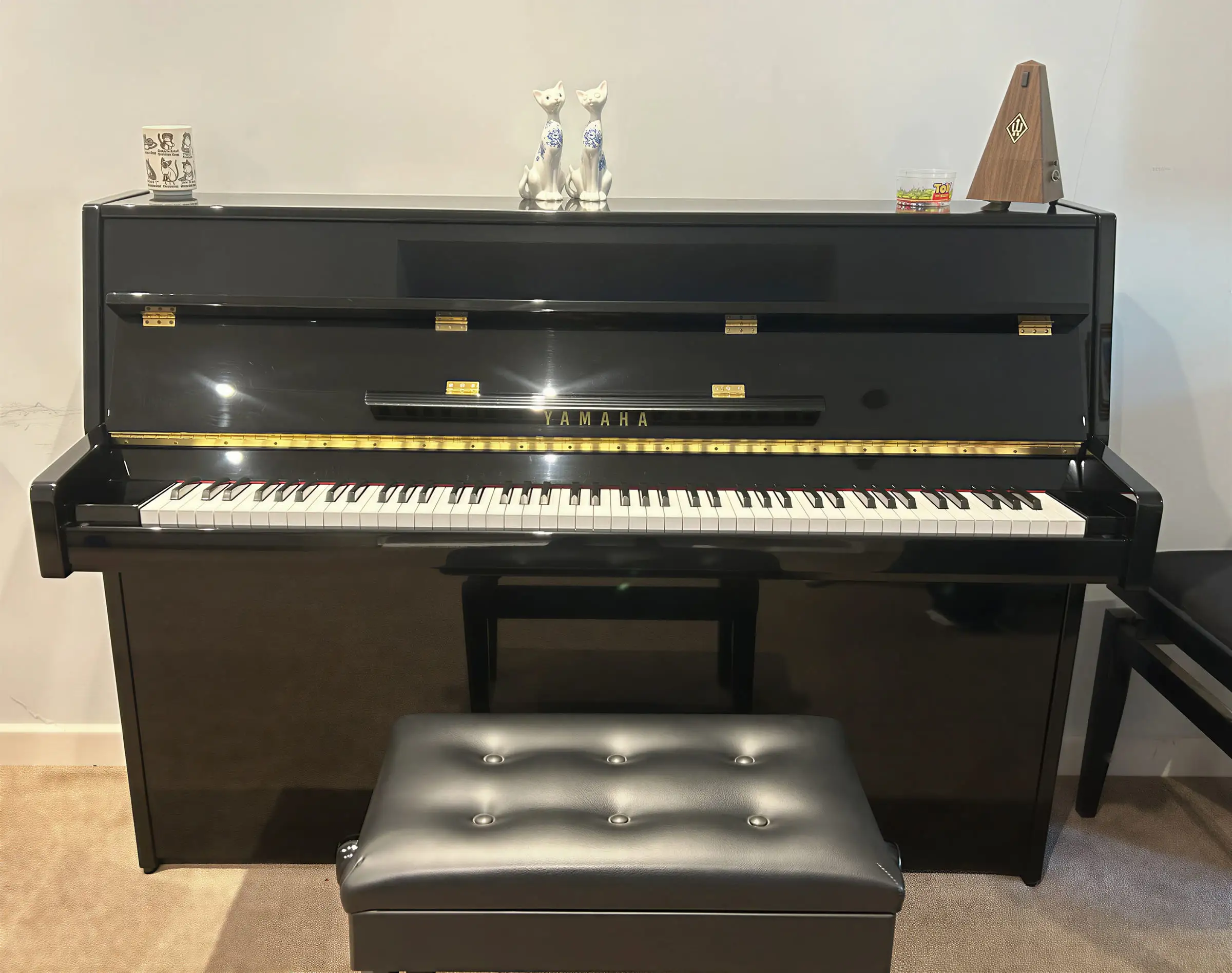 A black Yamaha upright piano standing against a wall with a stool in front of it